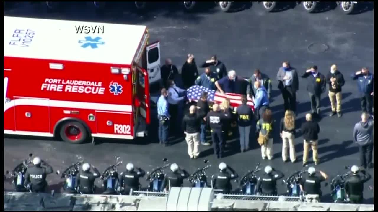 Aerial of U.S. flag draped over casket exiting back of ambulance after FBI shooting