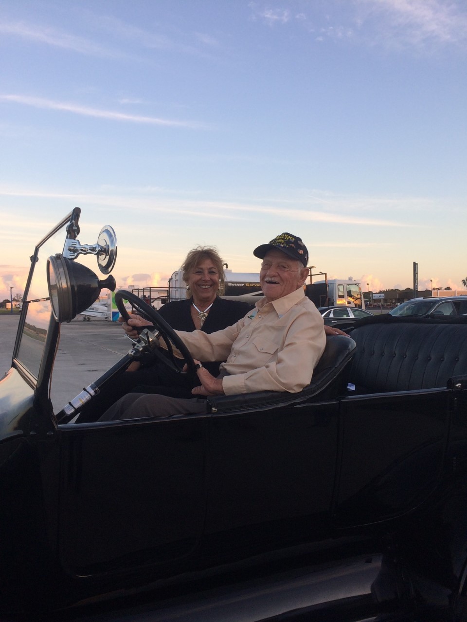 elderly man wearing white button up shirt riding a  black vintage convertible car.