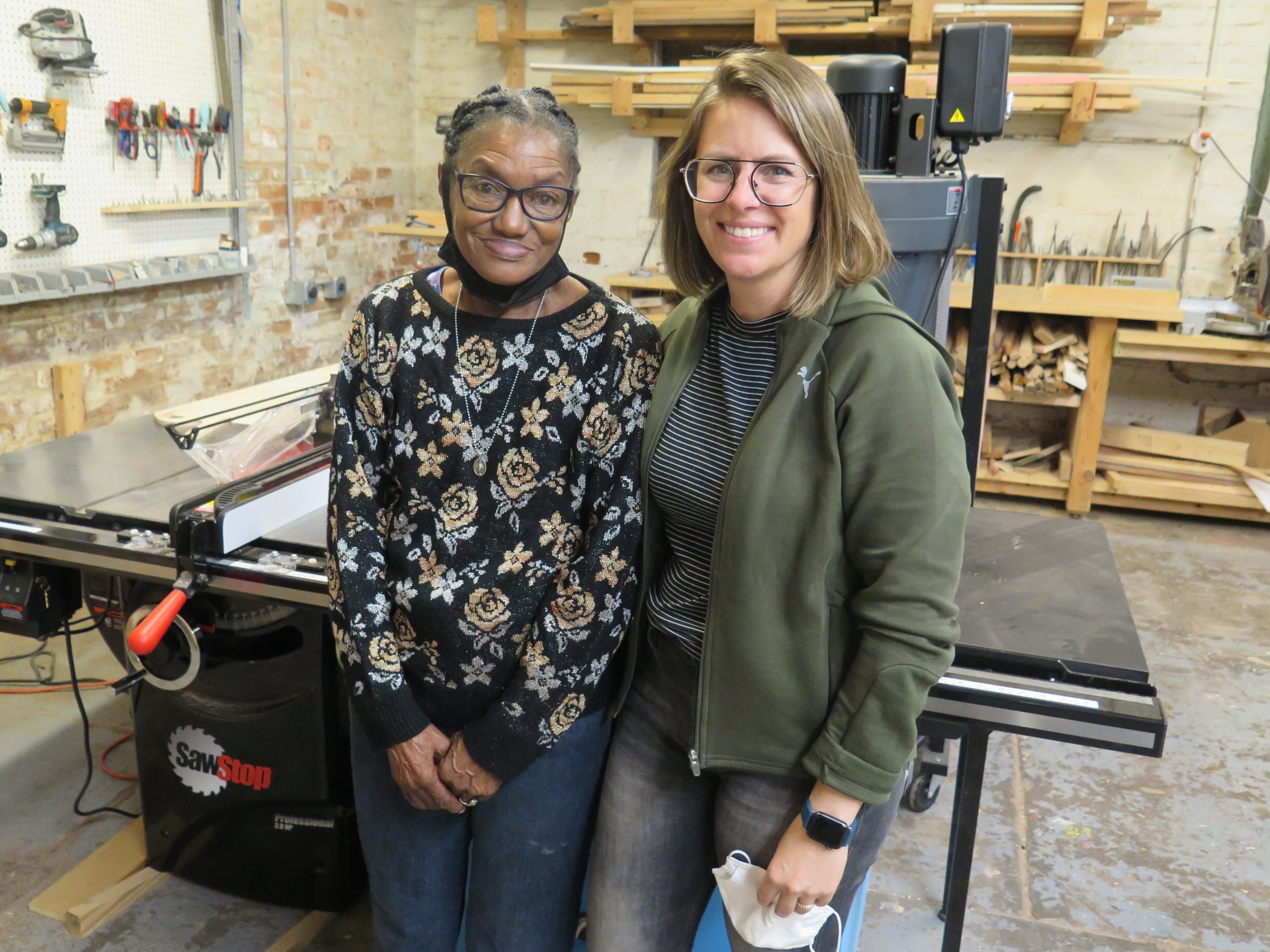 Johnnie Mae Gutter, left, and Lacey Haslam pose for a photo in Wave Pool wood shop in Camp Washington. Both are smiling and wearing glasses. 