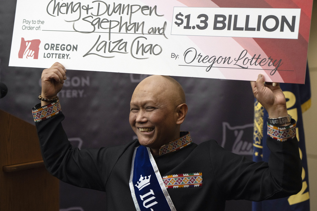 Oregon Powerball winner holds up his giant check.