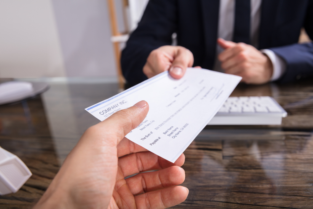 Close-up,Of,A,Businessperson's,Hand,Giving,Cheque,To,Colleague,At