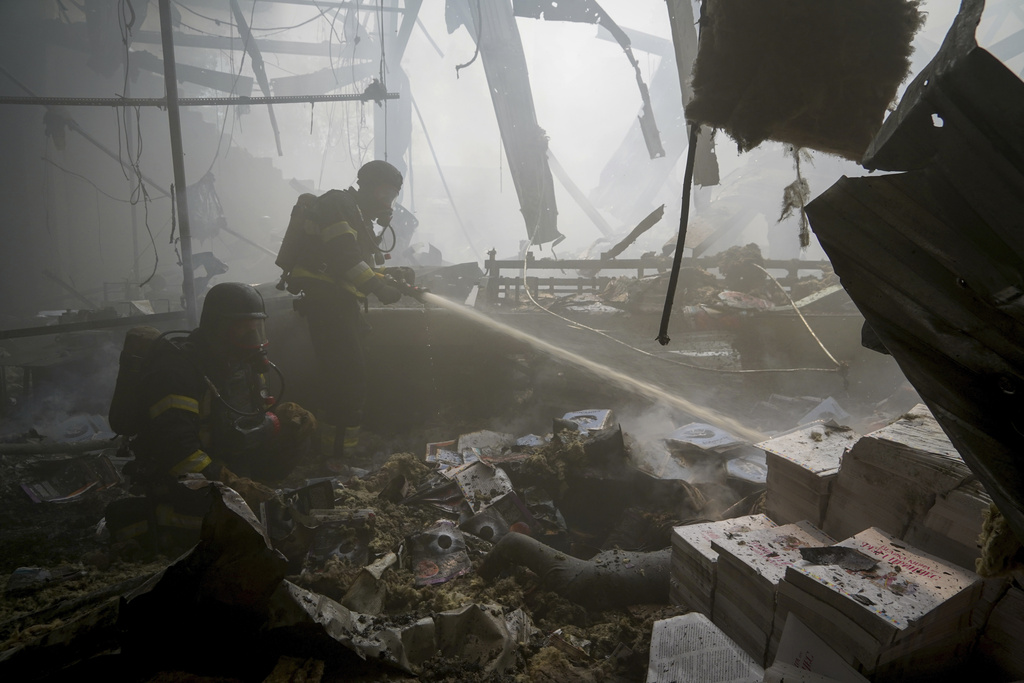 Firefighters hose down a fire as a lifeless body lies under the rubble after a Russian missile hit