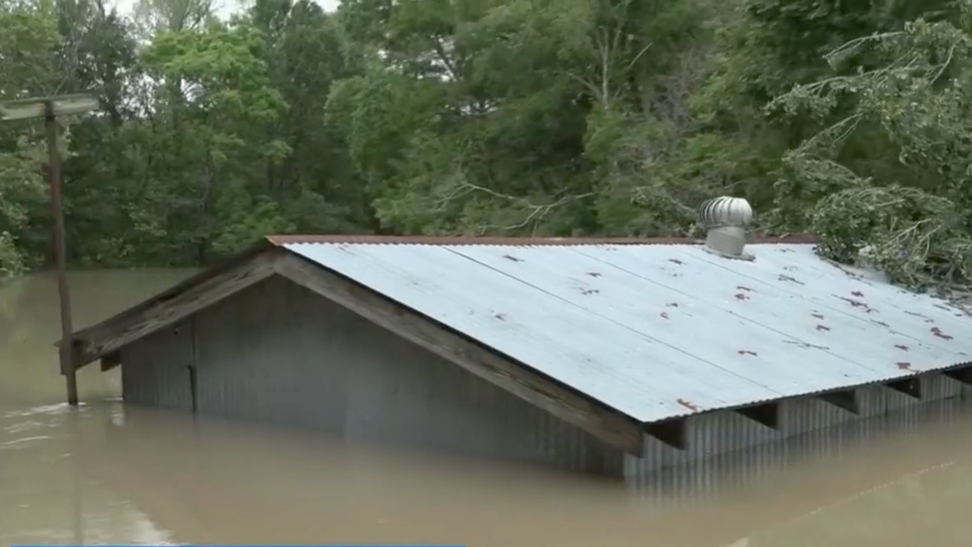 A home is flooded by rainwater, with only its roof visible.