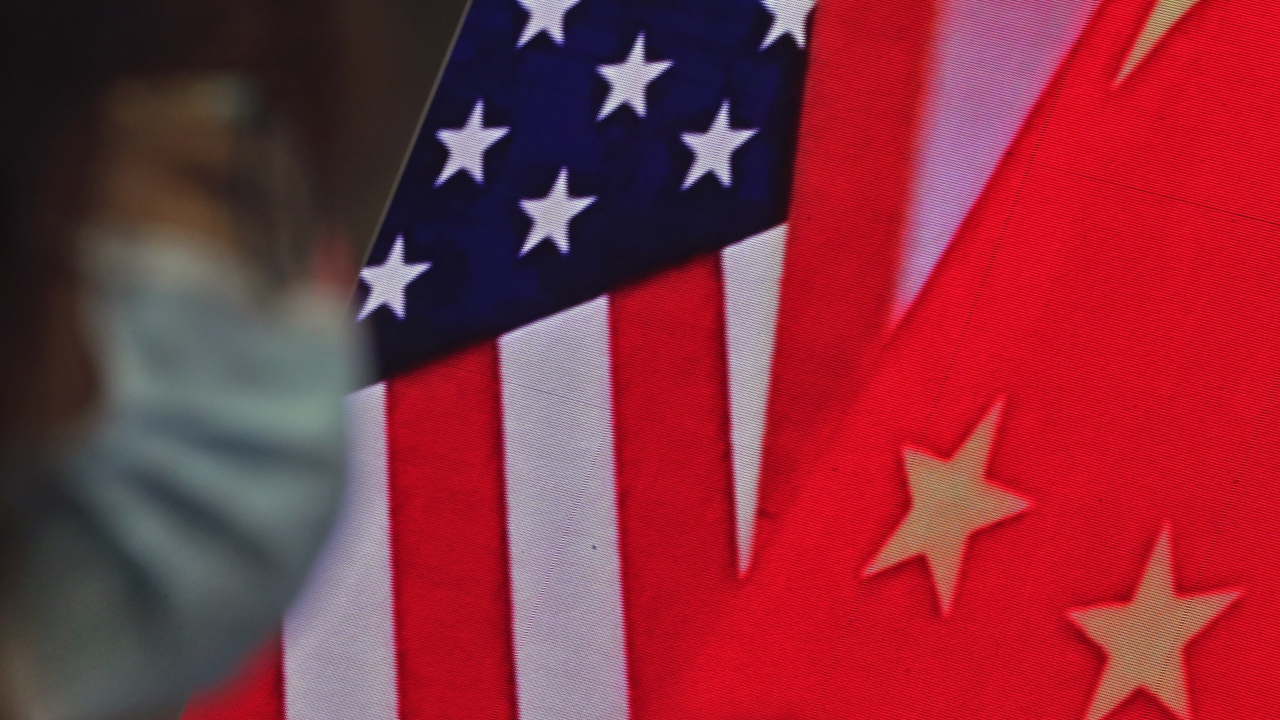A woman sits near a screen showing Chinese and U.S. flags.