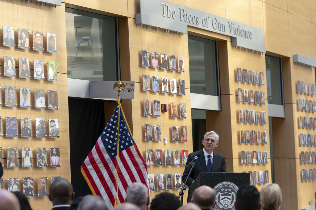 Attorney General Merrick Garland speaks next to a wall with photographs of victims of gun violence.
