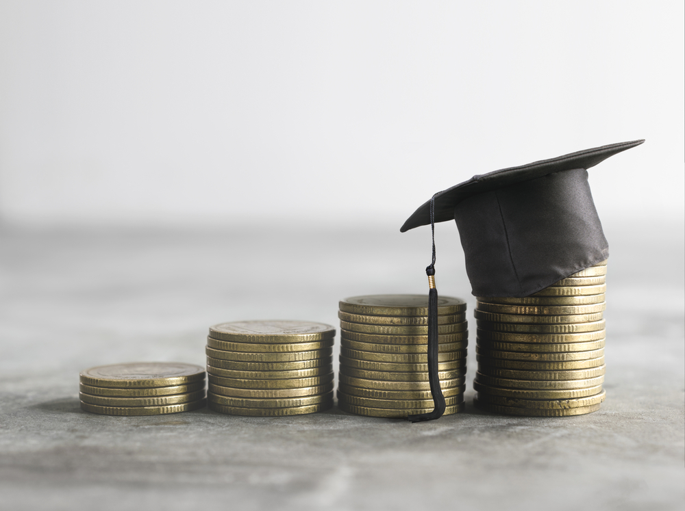 A graduation cap sits on a pile of coins.