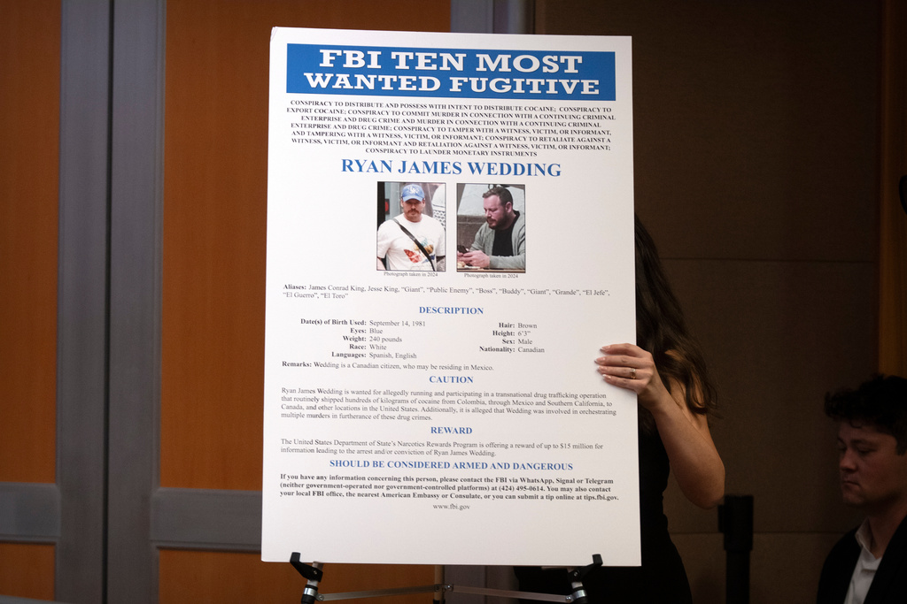 A staff member moves a wanted poster for Canadian fugitive Ryan James Wedding during a news conference at the Department of Justice, Wednesday, Nov. 19, 2025, in Washington.